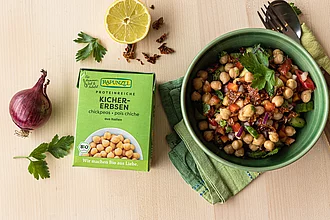 Fertig zubereitetes Gericht mit Kichererbsen, daneben ein Rapunzel TetraPak – stimmungsvolle Food-Inszenierung mit Bio-Hülsenfrüchten.