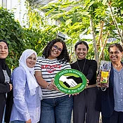 Gruppenfoto im Tropenhaus von Rapunzel mit CCF-Gründerin Samia Chibani. Mit im Bild sind das HAND IN HAND-Logo und die Datteln, die von Rapunzel verkauft werden.