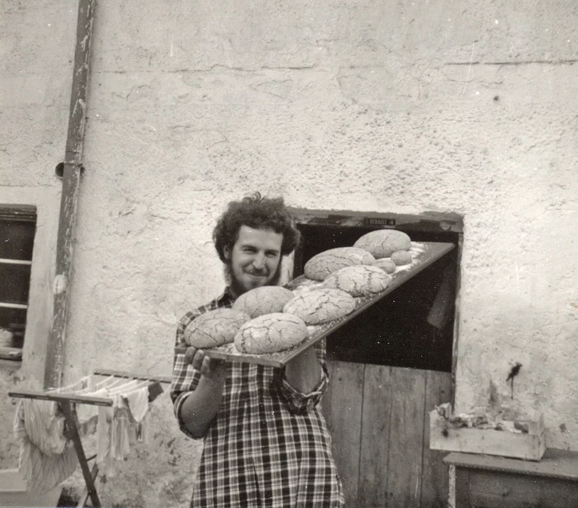 Ein Schwarz-Weiß-Bild zeigt Rapunzel Gründer Joseph Wilhelm in den 1970er Jahren mit selbstgebackenem Brot vor einem alten Backofen.