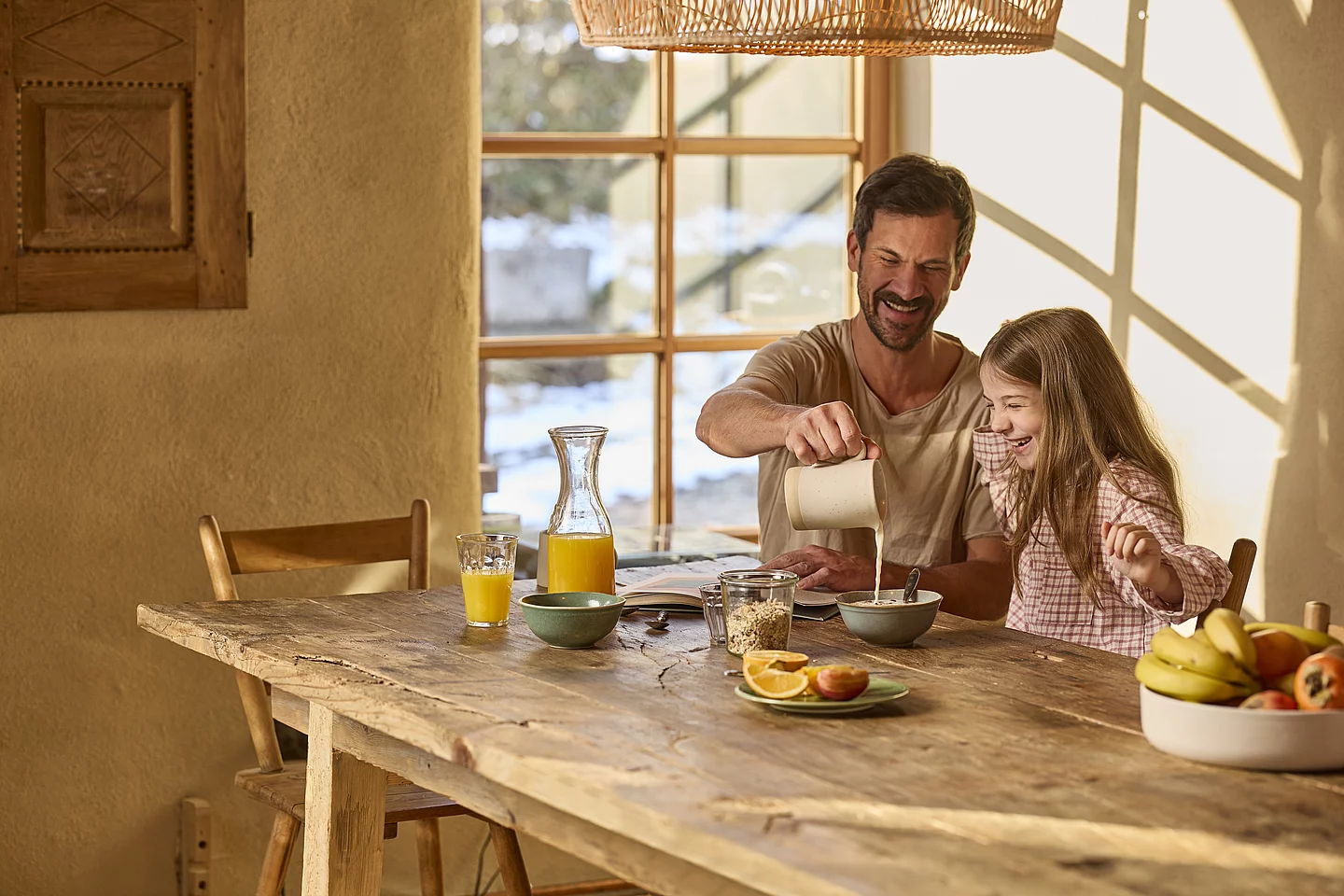 Gemeinsamer Frühstücksmoment mit Müsli Ein Vater und seine Tochter sitzen gemeinsam am Frühstückstisch. Der Vater schenkt Milch in die Müslischüssel des Kindes und bereitet das Frühstück zu.