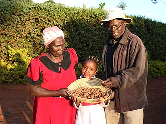 Eine Familie mit einem Kind hält geerntete Macadamia-Nüsse in die Kamera und wirkt glücklich. 