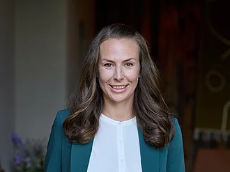 Rapunzel Geschäftsführerin Rosalie Dorn steht in einem Anzug in einem Türrahmen und lächelt in die Kamera  