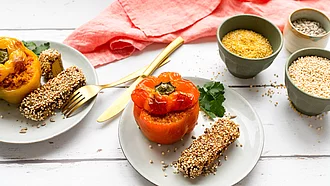 Mit Lupinenschrot gefüllte gelbe und orangene Paprika mit Räuchertofu auf Tellern angerichtet.