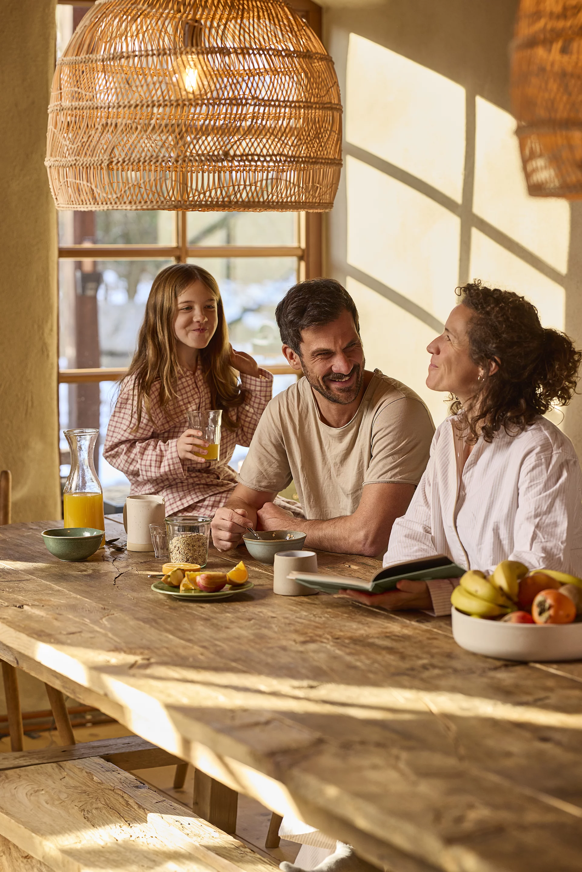 Gemeinsames Familienfrühstück. Eine Familie genießt gemeinsam ein Frühstück mit Müsli in einer ländlichen, bauernhofähnlichen Umgebung. Mutter, Vater und Kind sitzen zusammen am Frühstückstisch.