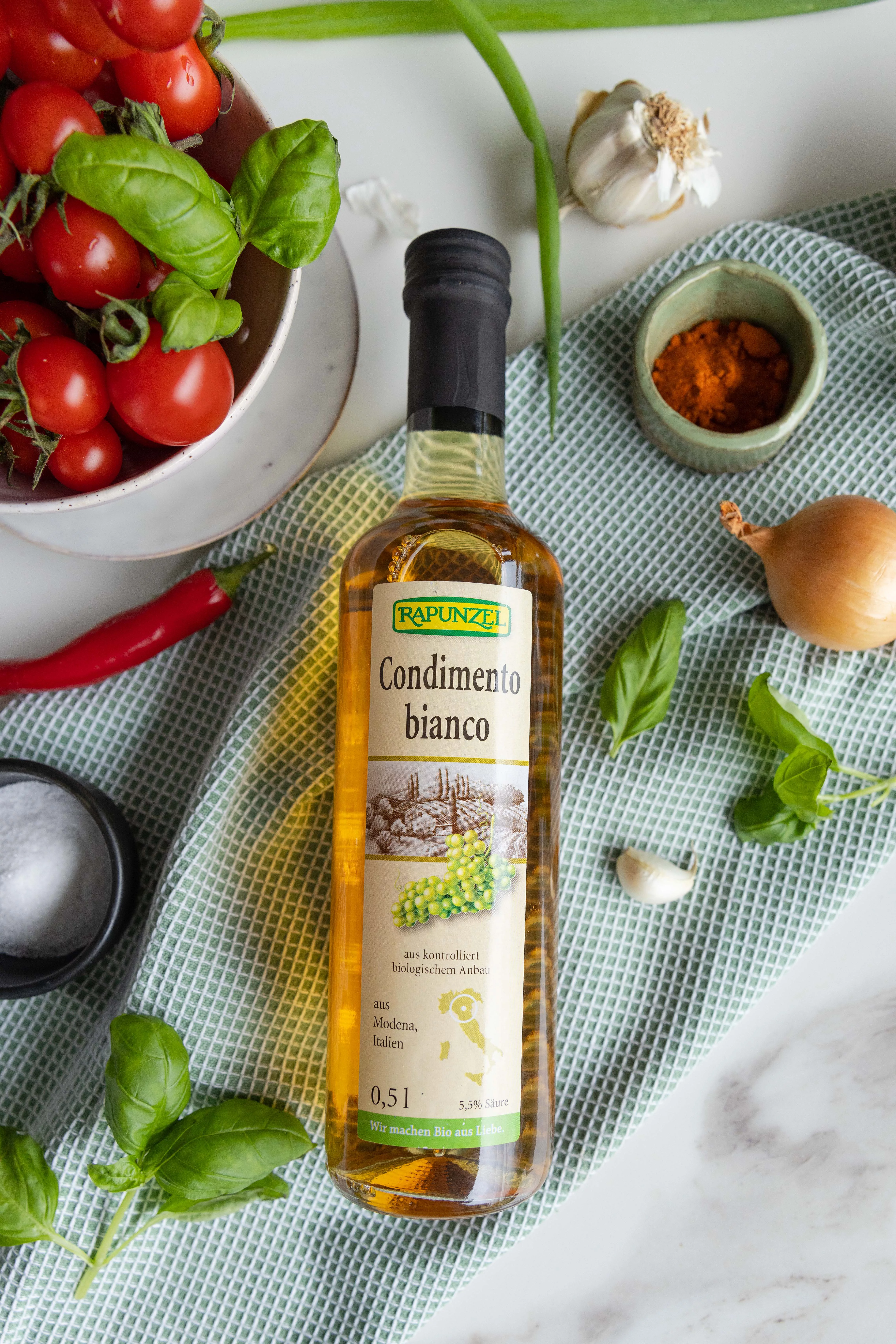 Conedimento bianco auf grünem Küchentuch umgeben von Gemüse wie Zwiebel, Knoblauch, Tomaten