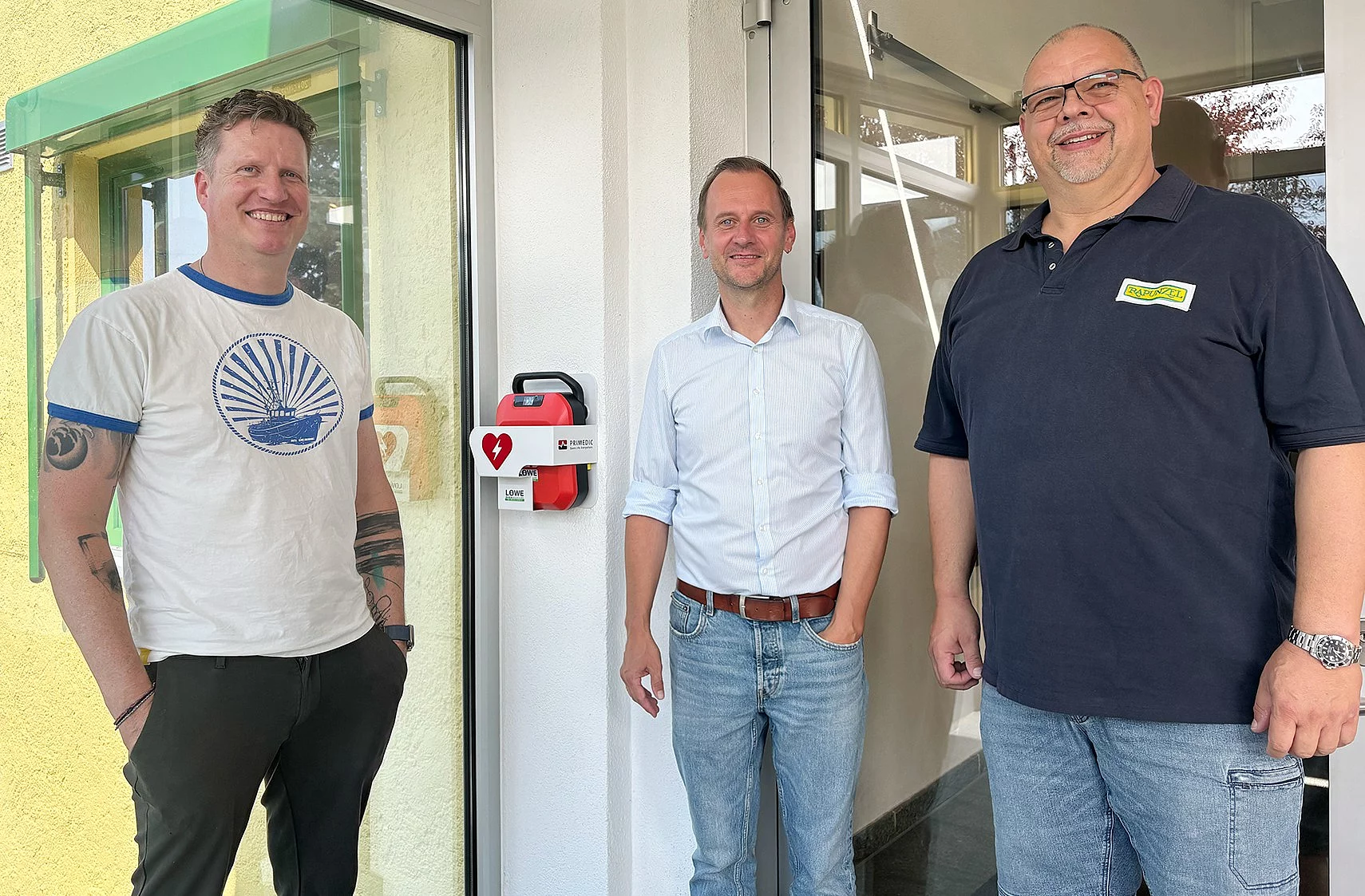 Neuer Defibrillator in Legau bei Rapunzel installiert. Stefan Schmaus, Geschäftsführer Rapunzel, Bürgermeister von Legau Thomas Heinle und der Leiter des Gebäudemanagements bei Rapunzel, Matthias Bloching mit dem neuen öffentlichen Defibrillator.