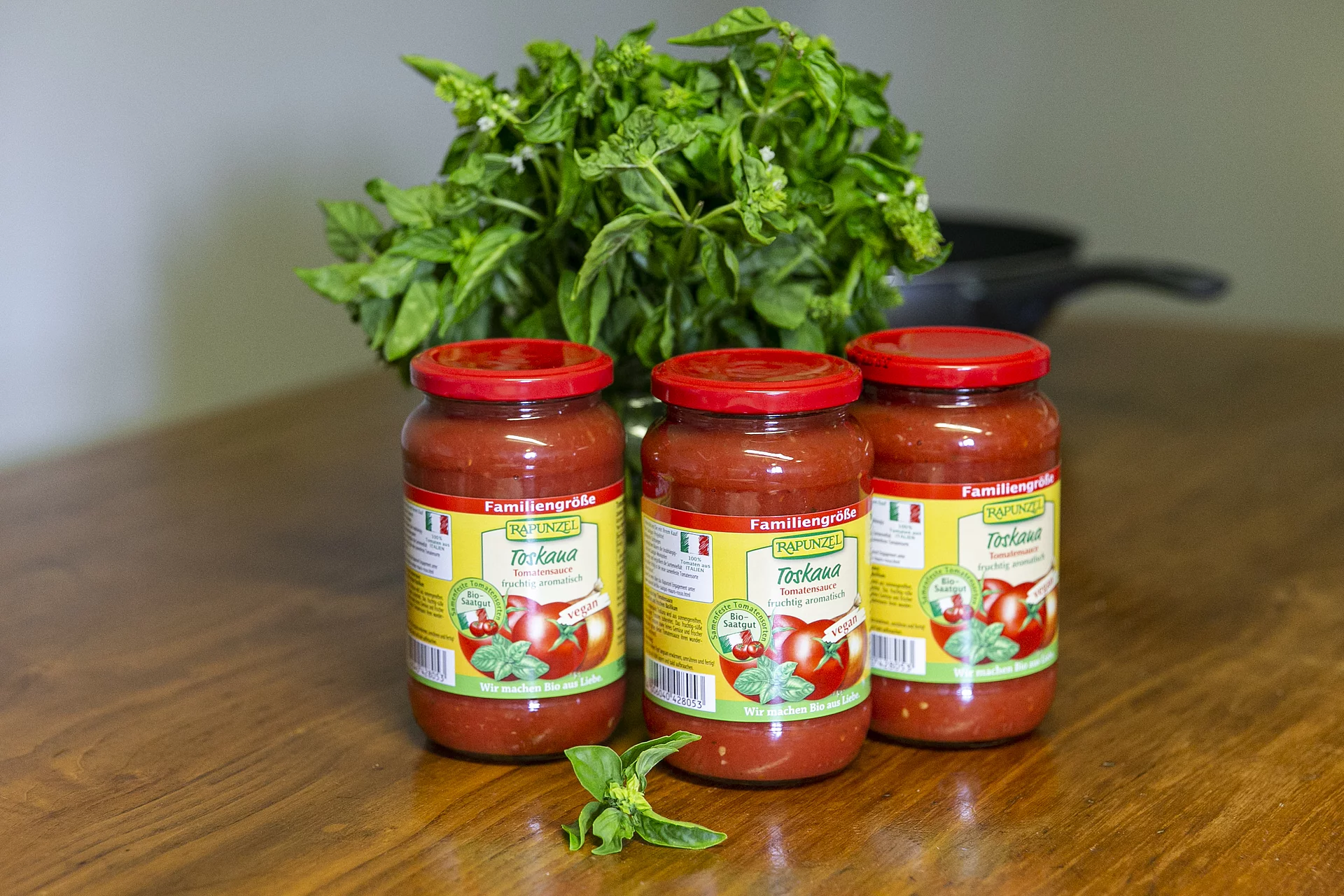 Rapunzel Toskana Tomatensauce drei Toskana Tomatensaucen vor einem Basilikum-Busch auf einem Holztisch