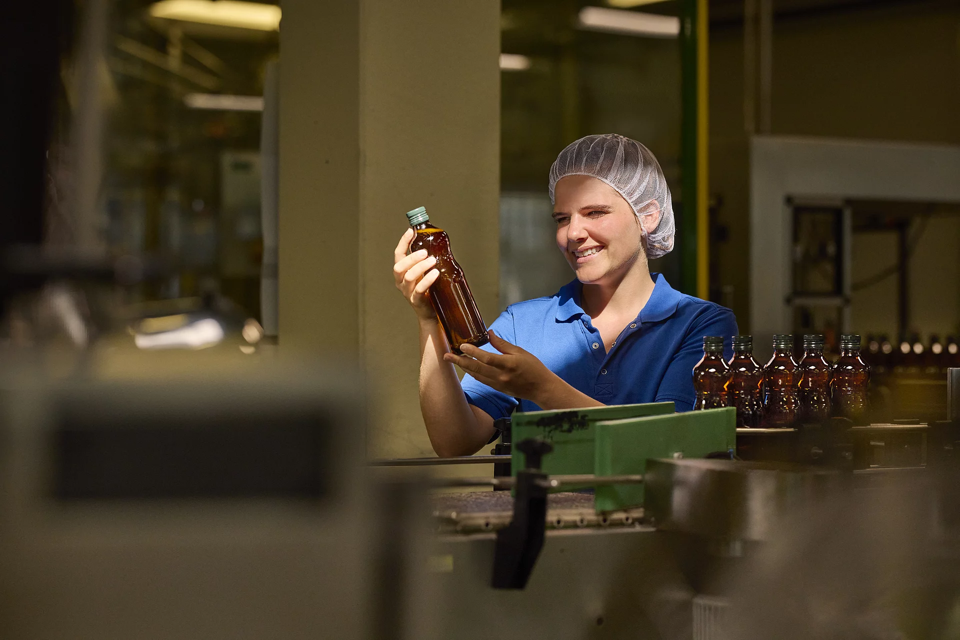 Rapunzel Olivenöl-Produktion – Qualitätsprüfung in der Lichtkontrolle. Rapunzel Mitarbeiterin hält eine Flasche Bio-Olivenöl ins Licht zur Qualitätskontrolle in der Produktion.