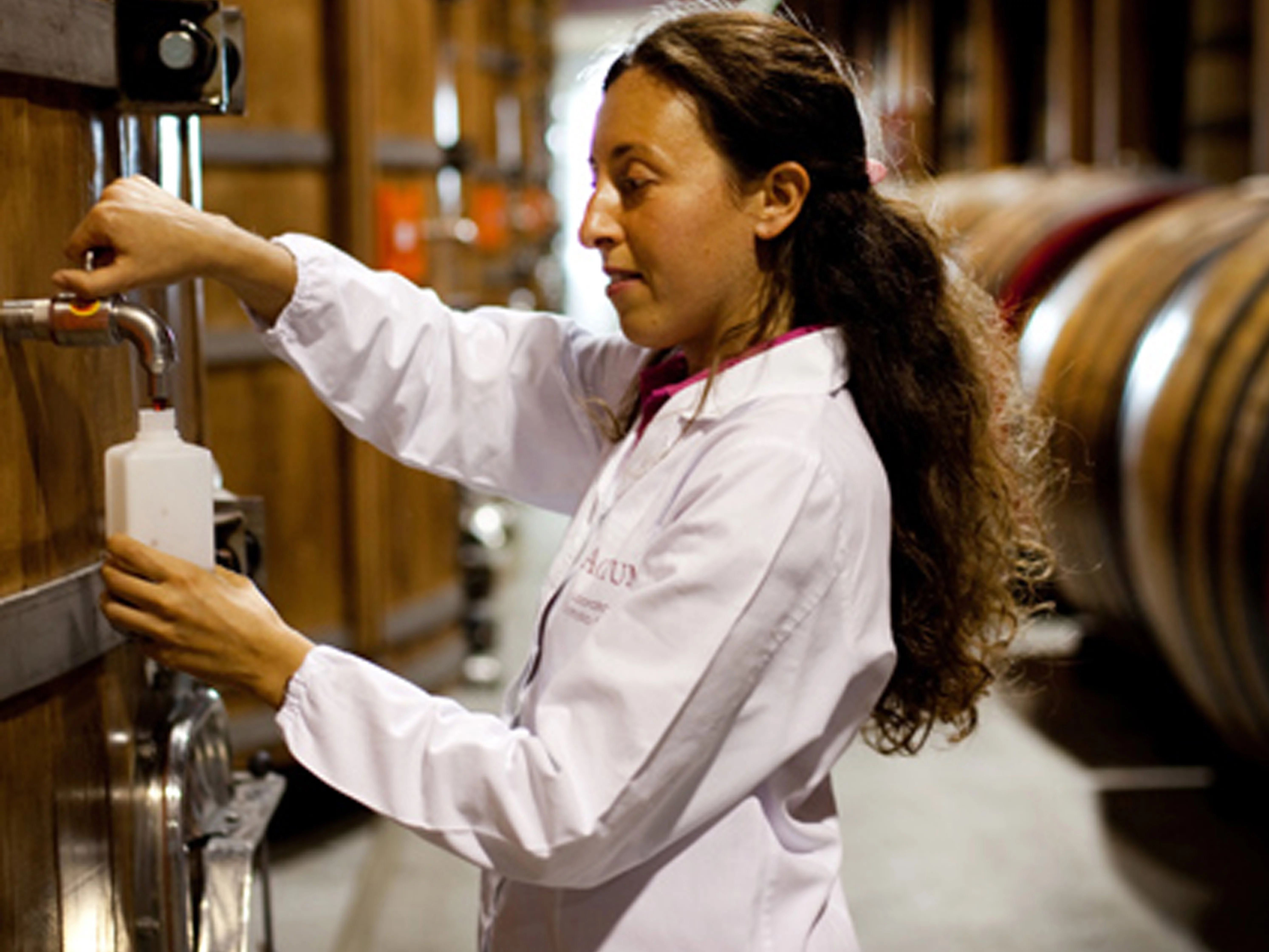 Im Vordergrund steht Kellermeisterin Chiara Nicoletti an einem Eichenfass und zieht eine Balsamico-Probe, im Hintergrund sind viele große Holzfässer zu sehen.