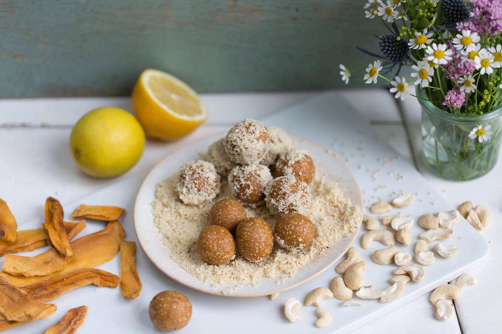 Fruchtkugeln aus Erdmandeln auf einem Teller, daneben die Zutaten Mango und Cashewkerne.