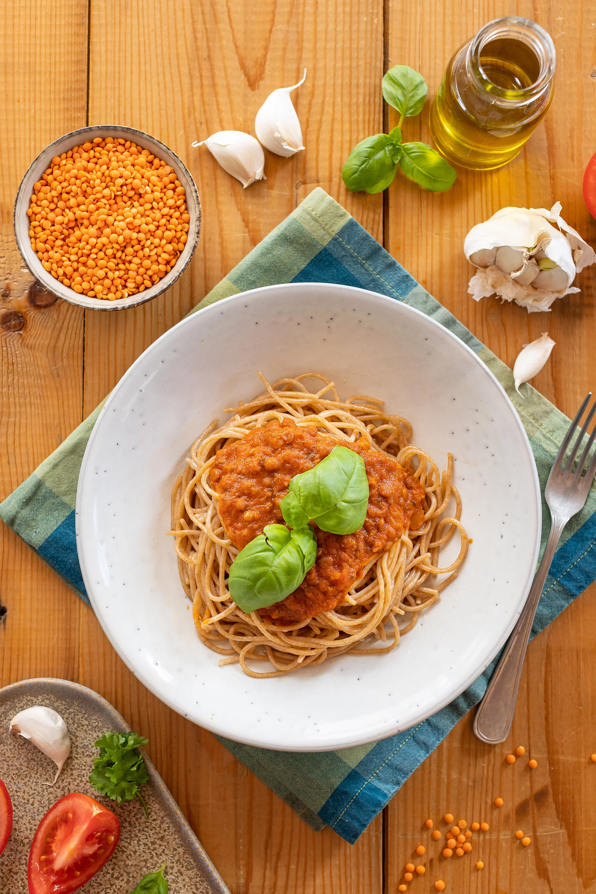 Ein weißr Teller mit Spaghetti und Linsenbolognese auf einem rustikalen Holztisch mit Kräutern