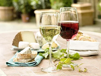 Weißweinglas neben Rotweinglas, dahinter Käse und Brot.