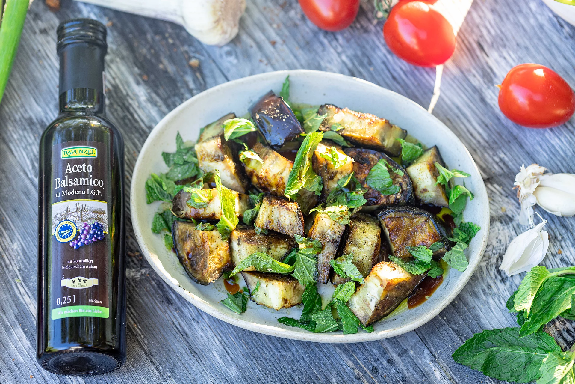 Balsamico ist ideal für Antipasti zum Grillen. Teller mit marinierten Auberginen, Balsamico-Flasche liegt daneben.