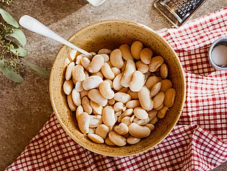 hale mit weißen Riesenbohnen als Rohware, umgeben von weiteren Zutaten für ein Gericht – stimmungsvolle Food-Inszenierung
