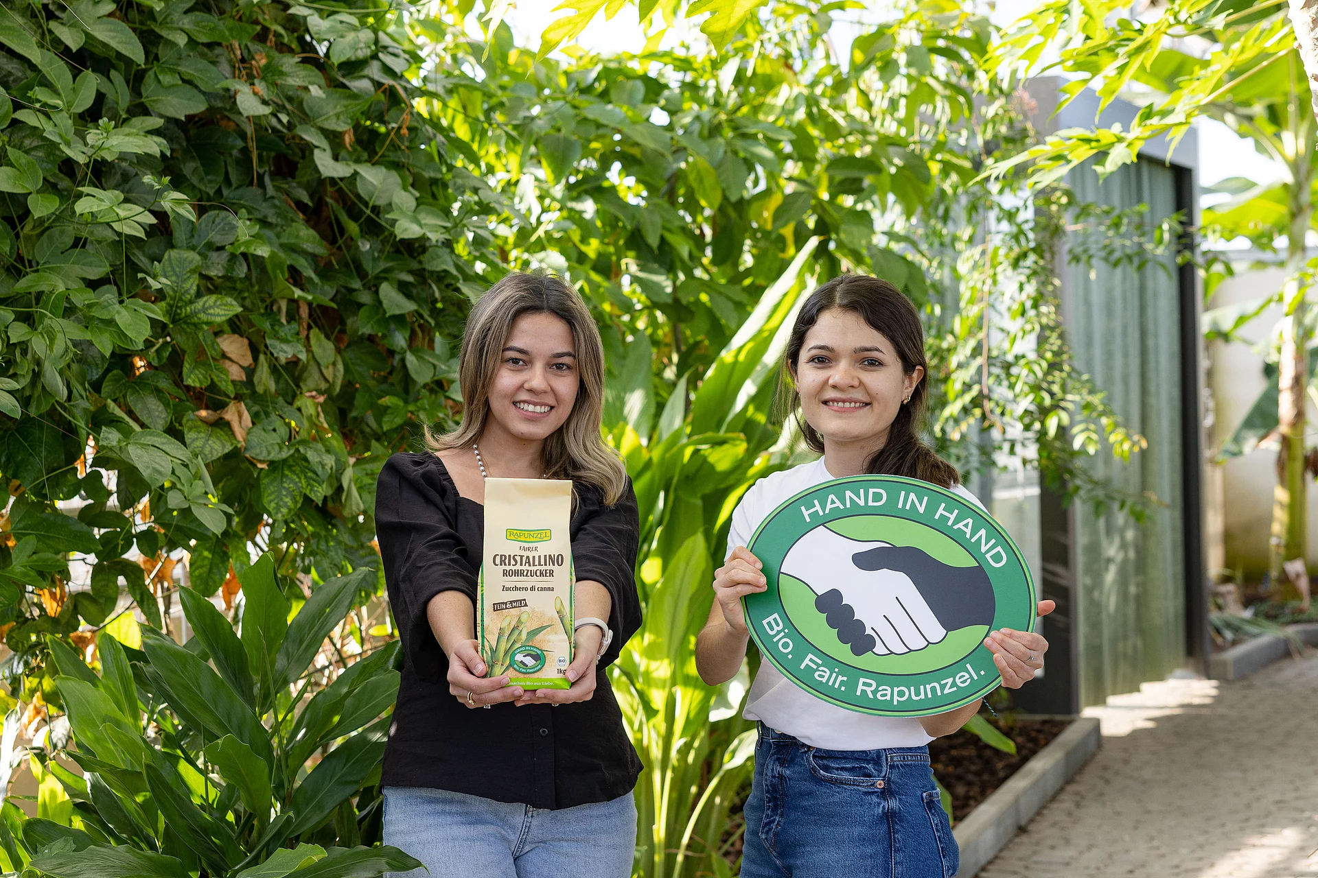 Die Leiterinnen des HAND IN HAND-Partners Manduvira mit Zuckerrohr, einer Packung Rohrzucker und dem HAND IN HAND-Logo.