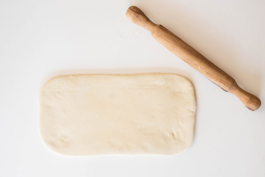 7. Den Hefeteig auf einer bemehlten Arbeitsfläche auf ein Rechteck mit etwa 35 x 20 cm ausrollen. Dabei die Ecken so gerade wie möglich halten. 7. Den Hefeteig auf einer bemehlten Arbeitsfläche auf ein Rechteck mit etwa 35 x 20 cm ausrollen. Dabei die Ecken so gerade wie möglich halten.